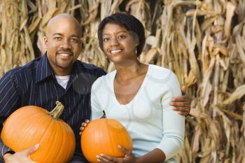 Royalty Free Photo of a Couple Sitting on Hay Bales and Holding Pumpkins at an Outdoor Market