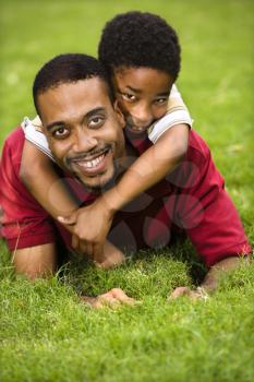 Royalty Free Photo of a Father Lying in the grass Smiling as a Son Climbs on His Back and Hugs His Neck