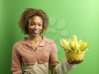 Royalty Free Photo of a Woman Standing Against a Green Background Holding a Bowl Full of Ears of Corn