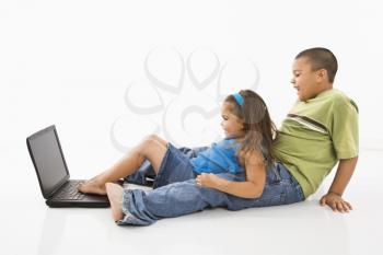 Royalty Free Photo of a Brother and Sister Putting Their Feet on a Laptop Computer and Smiling