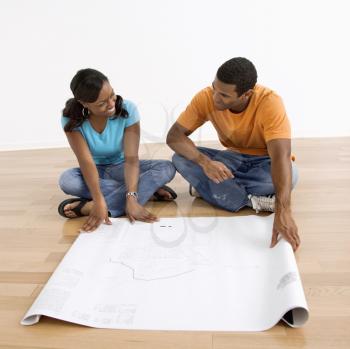 Royalty Free Photo of a Couple Sitting on the Floor Looking at Blueprints
