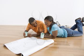 African American male and female couple lying on floor looking at architectural  blueprints.