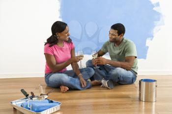 Royalty Free Photo of an African American Couple Sitting and Relaxing With Wine By a Half Painted Wall
