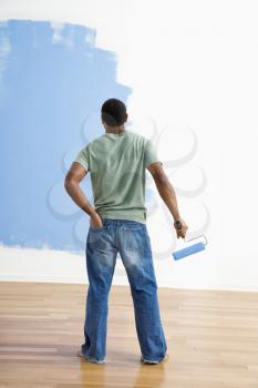 Royalty Free Photo of a Man Standing Next to a Half-painted Wall Holding a Paint Roller