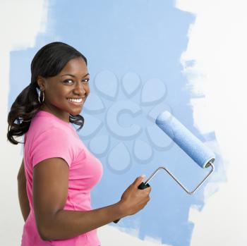 Royalty Free Photo of an  African American Woman Painting a Wall Blue and Smiling