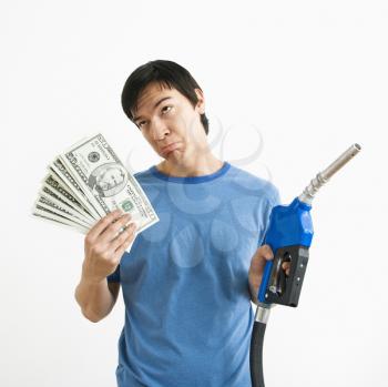 Asian young man with sad expression holding money and gas pump nozzle.