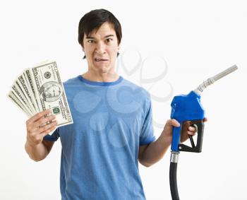 Asian young man with confused expression holding money and gas pump nozzle.