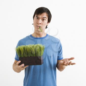 Royalty Free Photo of an Asian Young Man Standing Holding a Pot of Grass