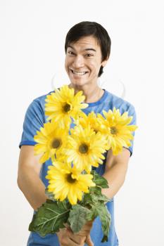 Asian young man holding bouquet of yellow gerber daisies smiling.
