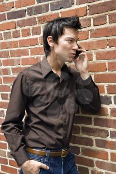 Royalty Free Photo of a Young Asian Man Next to a Brick Wall Talking on a Cellphone
