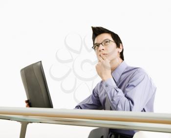 Asian businessman sitting at desk working on laptop thinking.