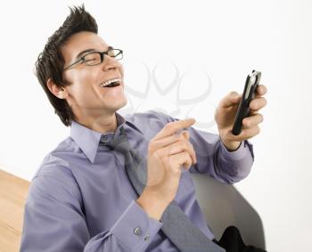 Royalty Free Photo of a Laughing Businessman Sitting at a Desk Texting Using His PDA Cellphone