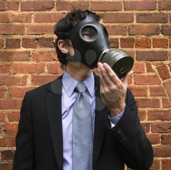 Royalty Free Photo of a Businessman Standing Next to a Brick Wall and Looking off to the Side Wearing a Gas Mask