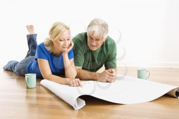 Royalty Free Photo of a Couple Lying on the Floor Looking and Discussing Architectural Blueprints