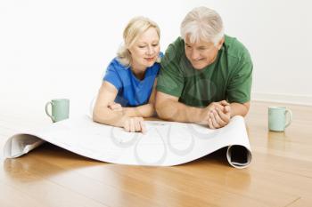 Royalty Free Photo of a Middle-aged Couple Lying on a Floor Looking at and Discussing Architectural Blueprints 