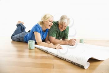 Royalty Free Photo of a Couple Lying on the Floor Looking and Discussing Architectural Blueprints