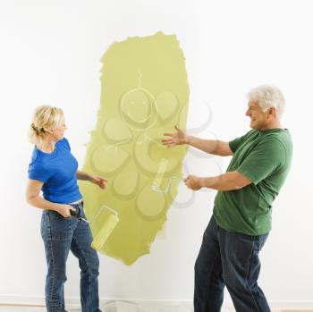 Middle-aged couple painting wall green finger-painting smiley face figurine for fun.