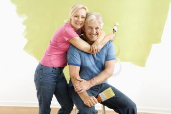 Royalty Free Photo of a Portrait of a Smiling Couple Sitting in Front of a Half-Painted Wall With Paintbrushes