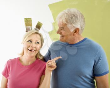Royalty Free Photo of a Couple Standing in Front of a Wall While a Man Makes Bunny Ears With Paintbrushes
