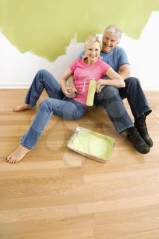 Royalty Free Photo of a Couple Sitting in Front of a Half-Painted Wall with Paint Supplies Snuggling