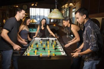 Group of young men and women enjoying a game of foosball in a bar.  Horizontal shot.