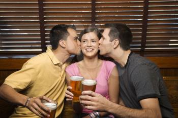 Two young men kissing a females cheek while holding their beers at a pub. Horizontal shot.