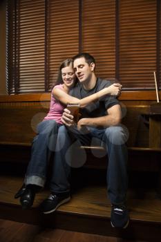 Man and woman embracing on a bench while relaxing at a pub. Vertical shot.