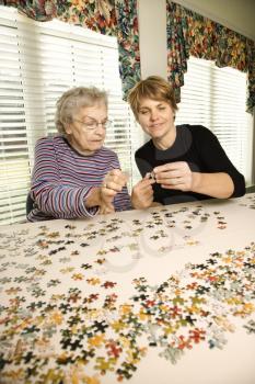 Elderly woman and younger woman work on a jigsaw puzzle together.  Vertical shot.
