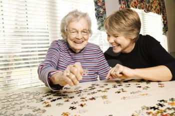 Elderly woman and a younger woman work on a jigsaw puzzle.  Horizontal shot.
