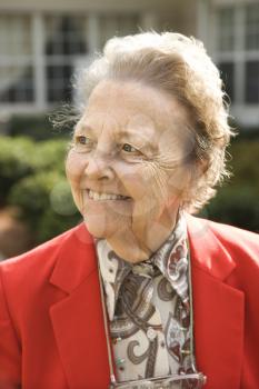 Portrait of elderly woman in red coat smiling to the side. Vertical shot.