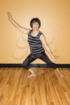 Asian woman stands with outstretched arms while performing a yoga position at the gym. Vertical shot.