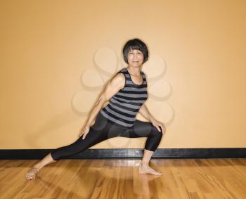 Asian woman stands in a yoga position with an outstretched leg at the gym. Horizontal shot.