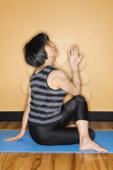 Asian woman practices yoga on an exercise mat at the gym. Vertical shot.