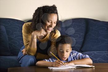 A mid adult African American woman sits on a couch and helps her young some with his homework. Horizontal shot.