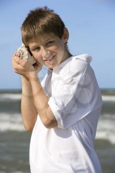 Boy listens to a shell at the beach. Vertical shot.