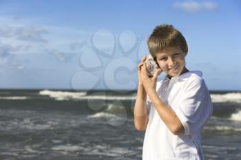 Boy listens to a shell at the beach. Horizontal shot.