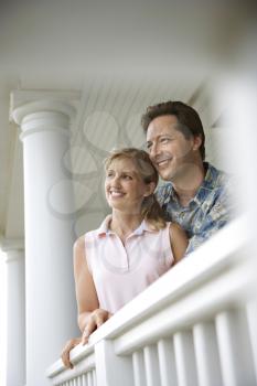 Smiling man and woman look out from a house porch, lean on a railing. Vertical shot.