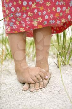 Closeup of a little girl's barefoot feet that are crossed and covered in sand. Vertical shot.