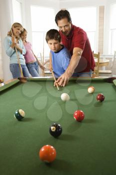 Man and boy playing pool with woman and girl in background. Vertically framed shot.