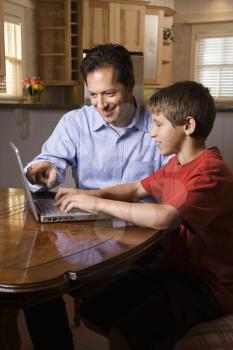 Father and son sitting at dining room table working on wireless laptop computer.