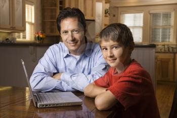 Father and son sitting at dining room table with wireless laptop computer.