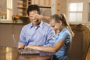 Young girl working on laptop at home covering man's face with hand. 
