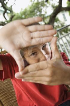 Young boy looking through hands at viewer.