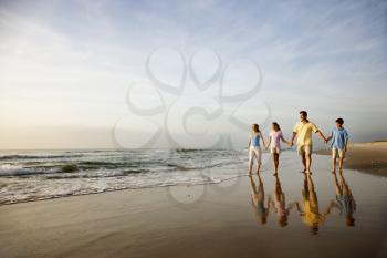 Family of four holding hands and walking on beach in North Carolina. 