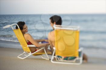 Man and woman smile at each other while sitting in beach chairs. Horizontal shot.
