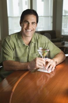 Man smiles at the camera while holding a martini. Vertical shot.