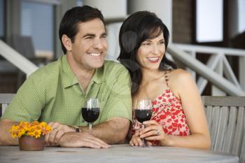 Man and woman are seated at an outdoor cafe, looking to the side while holding glasses of wine. Horizontal shot.