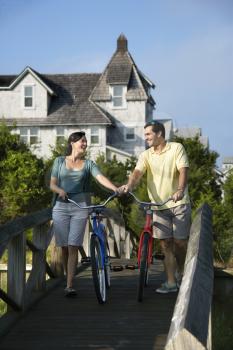 Smiling couple walking bikes across a bridge.  Vertical shot.