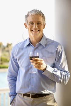 Portrait of a middle aged man on a terrace drinking red wine. Vertical shot.