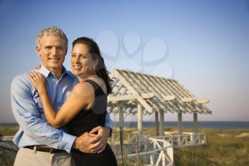 Couple embrace on the beach with arbor in background. Horizontal shot.